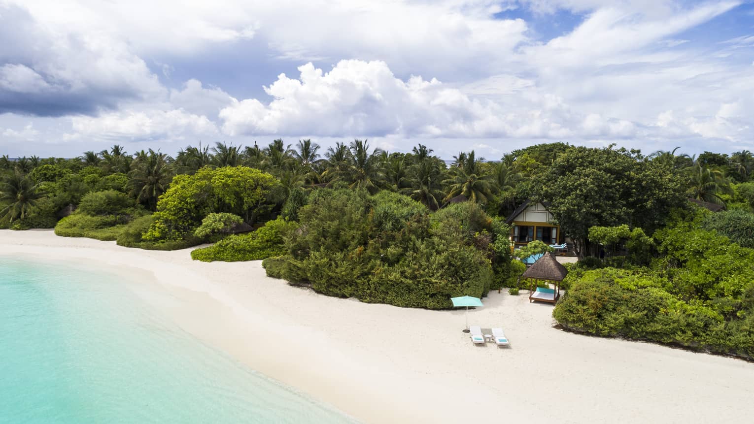Quiet white-sand beach in the Maldives with turquoise water and lush green trees inland