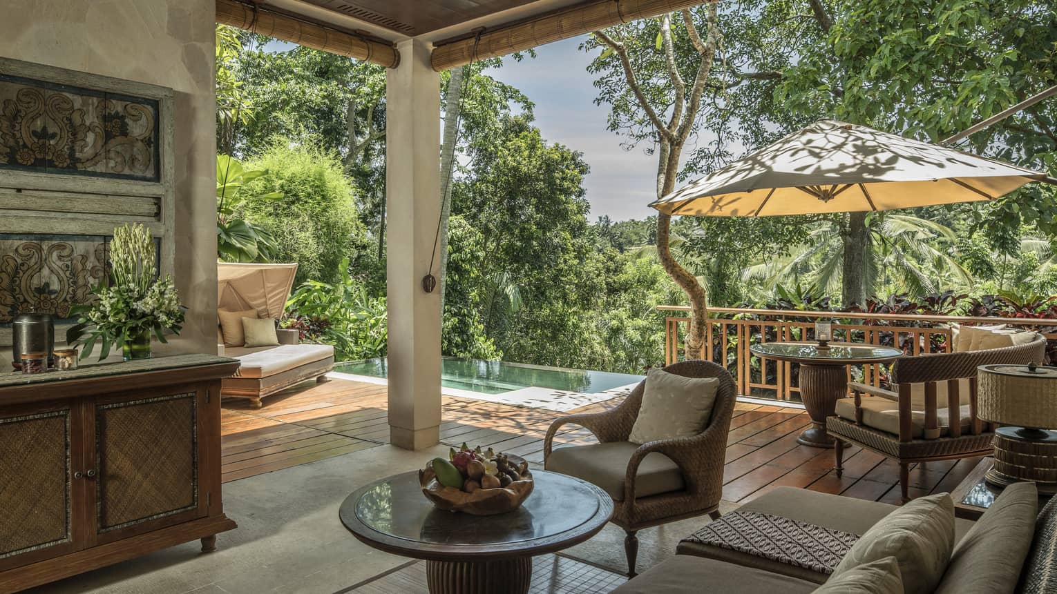 The covered patio of a villa, providing shade and a stunning view of a forest in Bali