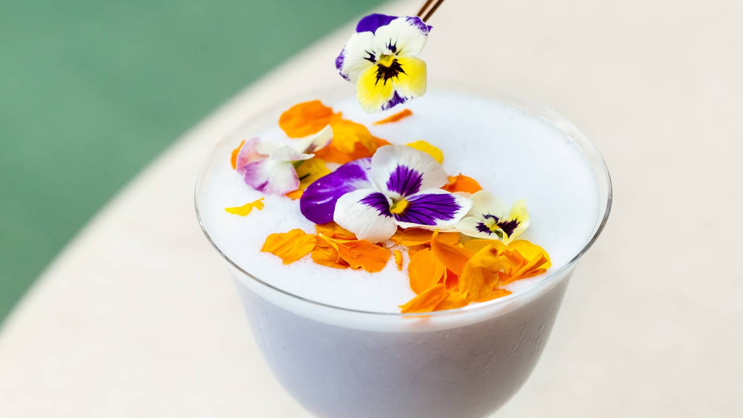 A stemmed glass of a white tropical cocktail topped with flowers 