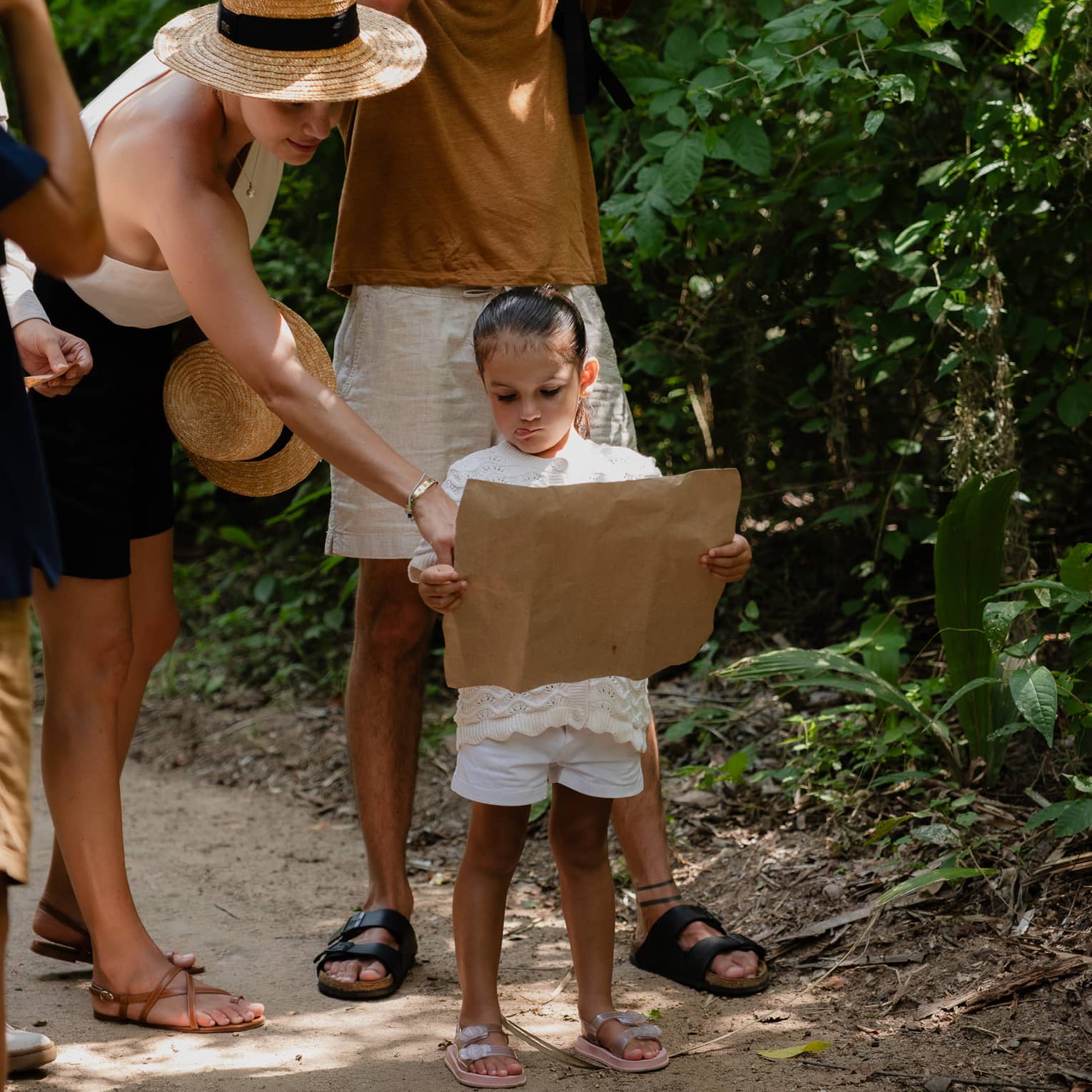 A group of people on a jungle trail. Two are consulting a map, and one is looking through binoculars.