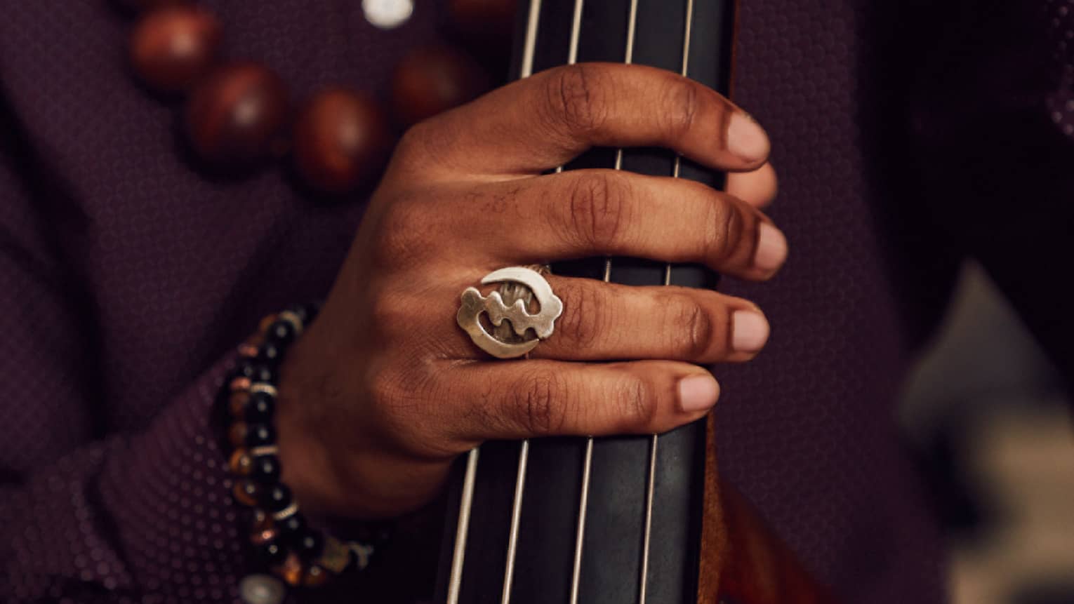 A dark skinned man holding a cello while wearing a maroon dress shirt.