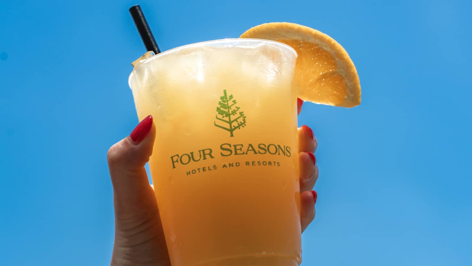 Guest holding orange drink with straw and orange slice on the glass.