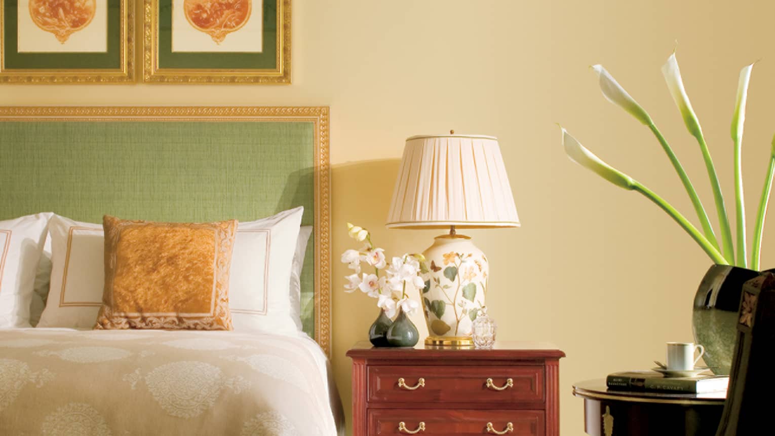 Close-up of Superior City-View Room bed with green headboard, gold frame and accent pillow, bedside lamp and orchid