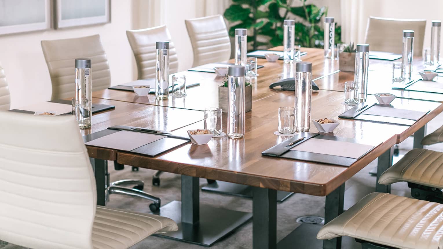 A rectangular boardroom table set with clear glass water bottles and black folders in a naturally-lit room