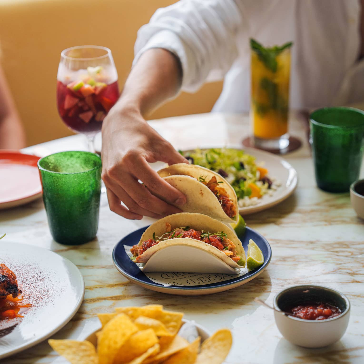 Person sitting at restaurant table reaches for a taco