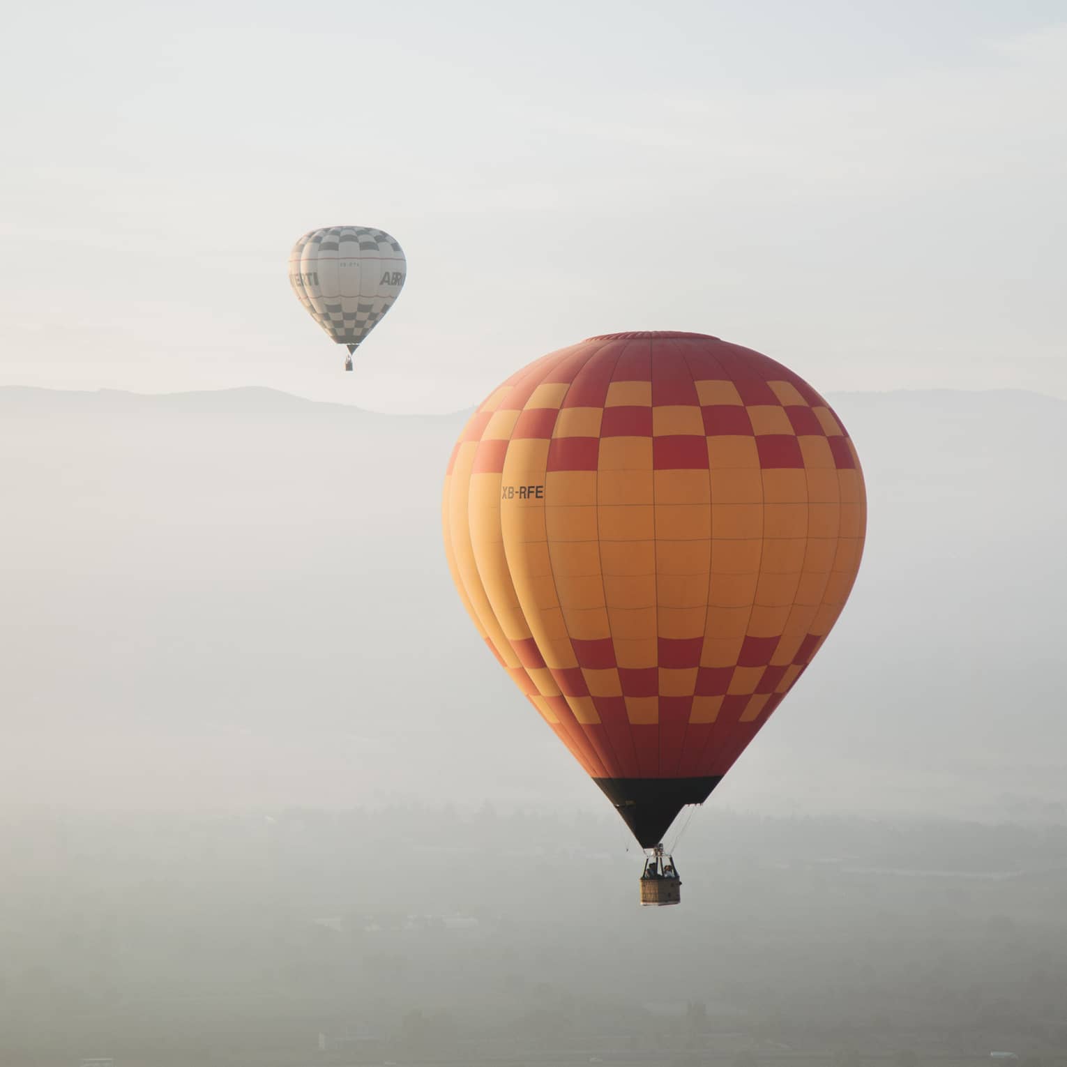 Yellow hot air balloon with red checkers in sky, hot air ballon in distance 