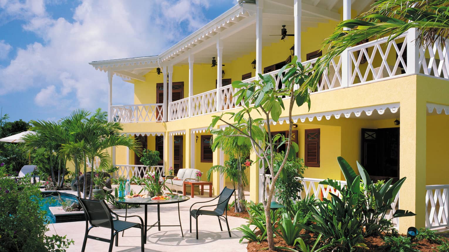 Sunset Hill Residence two-storey yellow villa with white trim balcony overlooking pool, patio