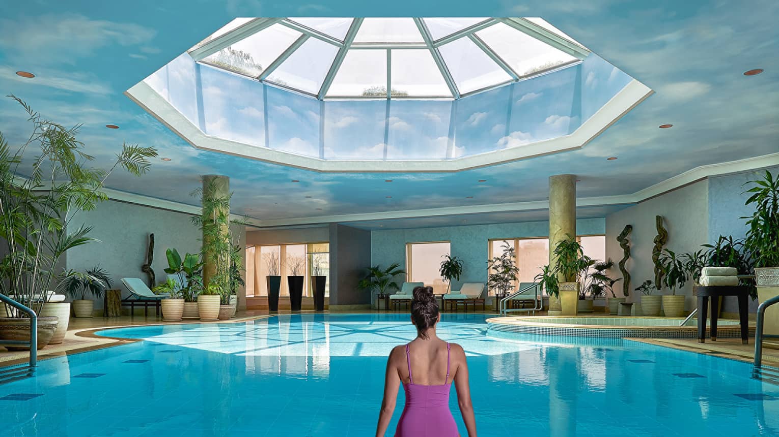 Woman in swimsuit seated on edge of indoor pool with blue ceiling and skylight above