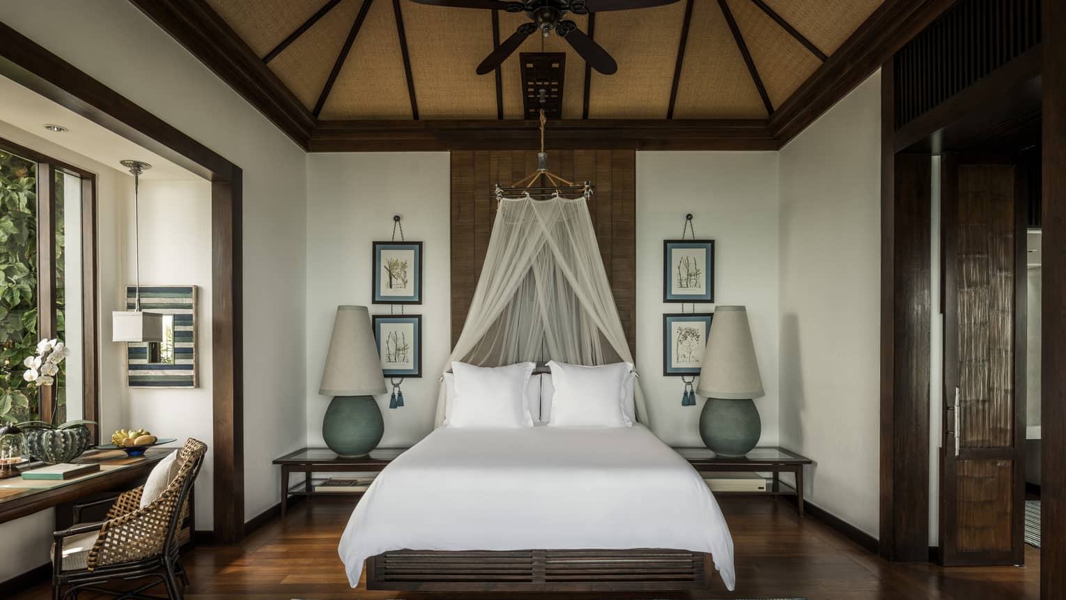Family Pool Villa bed with white net canopy, large lamps on each side, wood floors, desk by window