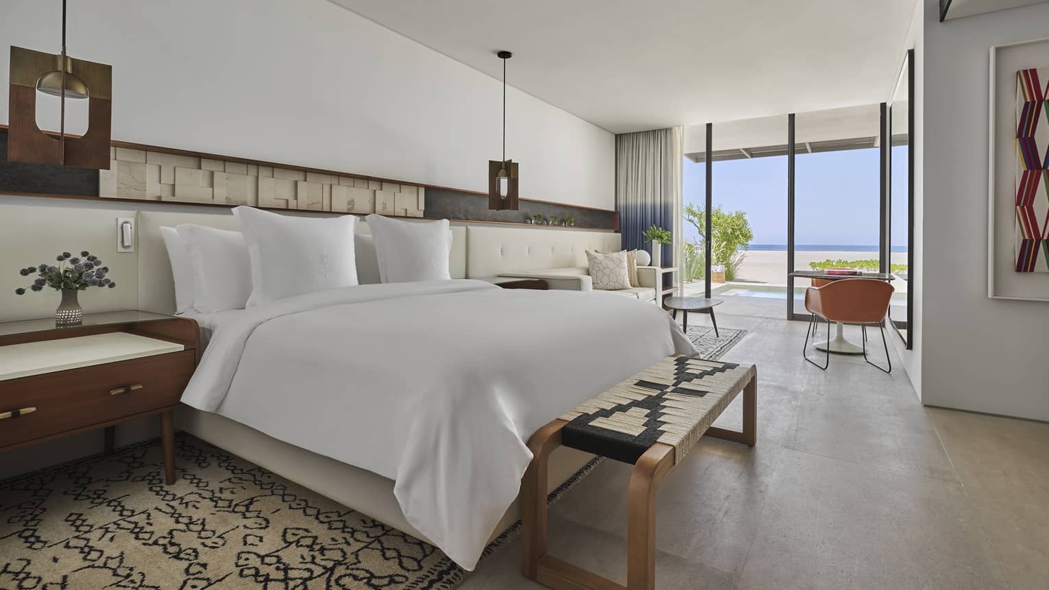 Two Bedroom Sunrise Suite bedroom with King bed, white linens, foot-of-the-bed bench, table for two, floor-to-ceiling window with two-tone curtains and ocean views