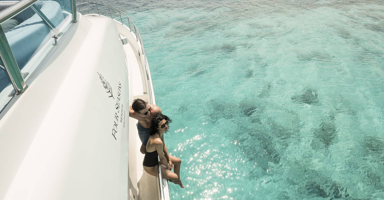A couple lounges on the side of a yacht in a blue lagoon