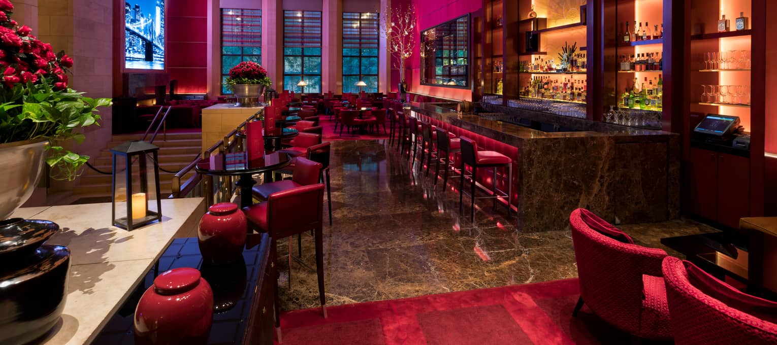 Ty Bar dining room with cocktail tables, red chairs, stools and area rug, three tall windows