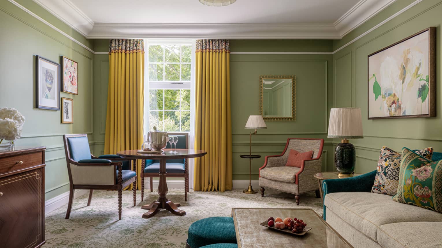 Guest room with cream couch and matching accent chair, coffee table, small round table for two, avocado-coloured walls, window with yellow drapes