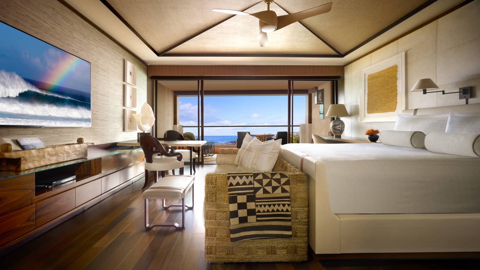 Hotel suite bed and sofa at foot facing TV, seating area with floor to ceiling window and ocean view