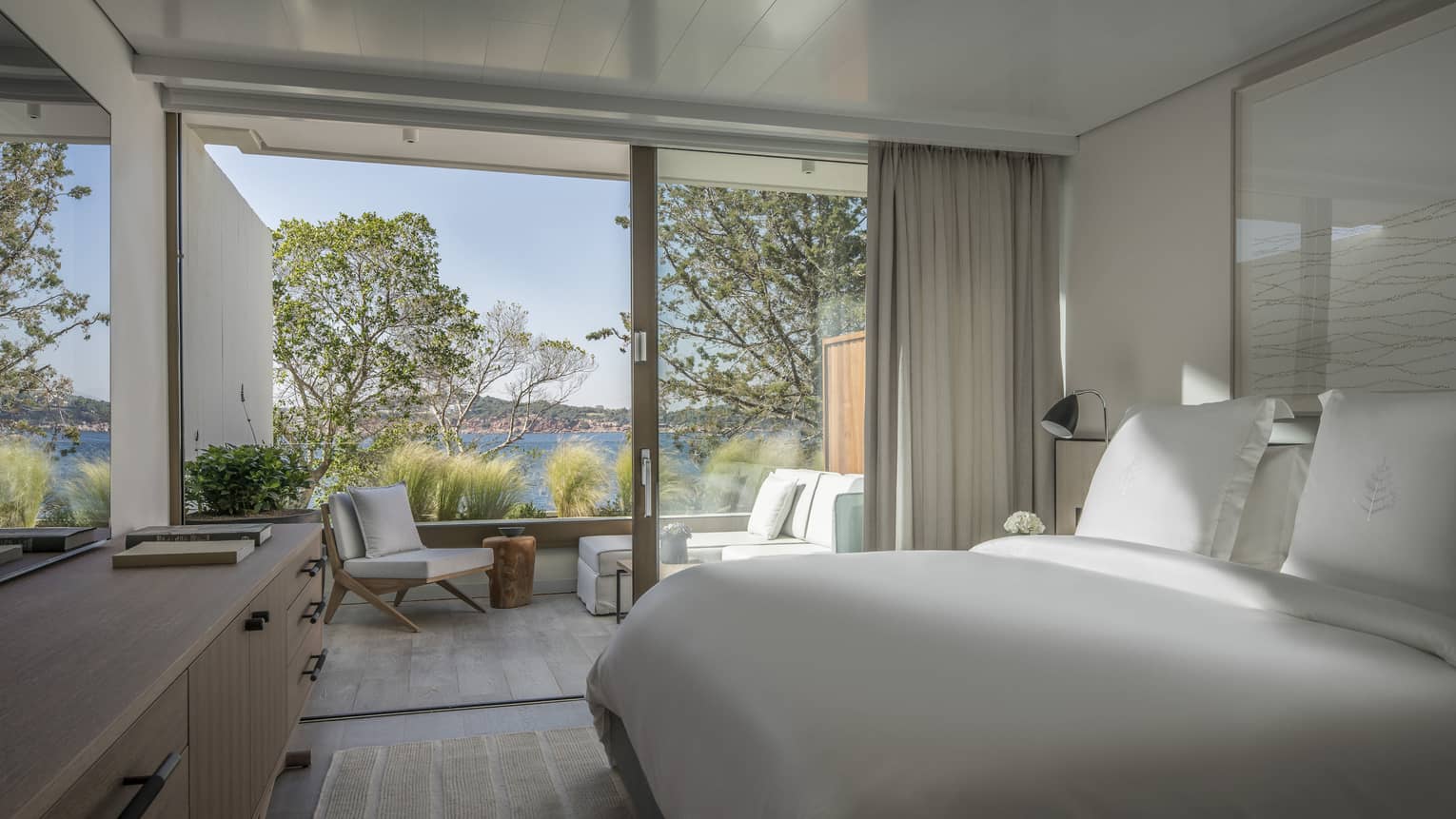 Sleek, Nafsika One Bedroom Terrace Suite with white furniture and bedding overlooking trees and ocean