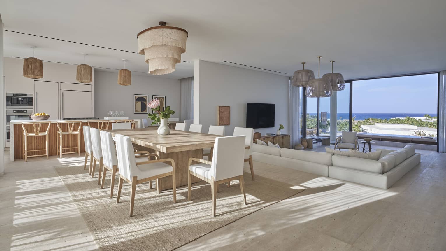 Modern open living area with dining table and white chairs, kitchen with barstools and sunken sectional facing tall windows and water view