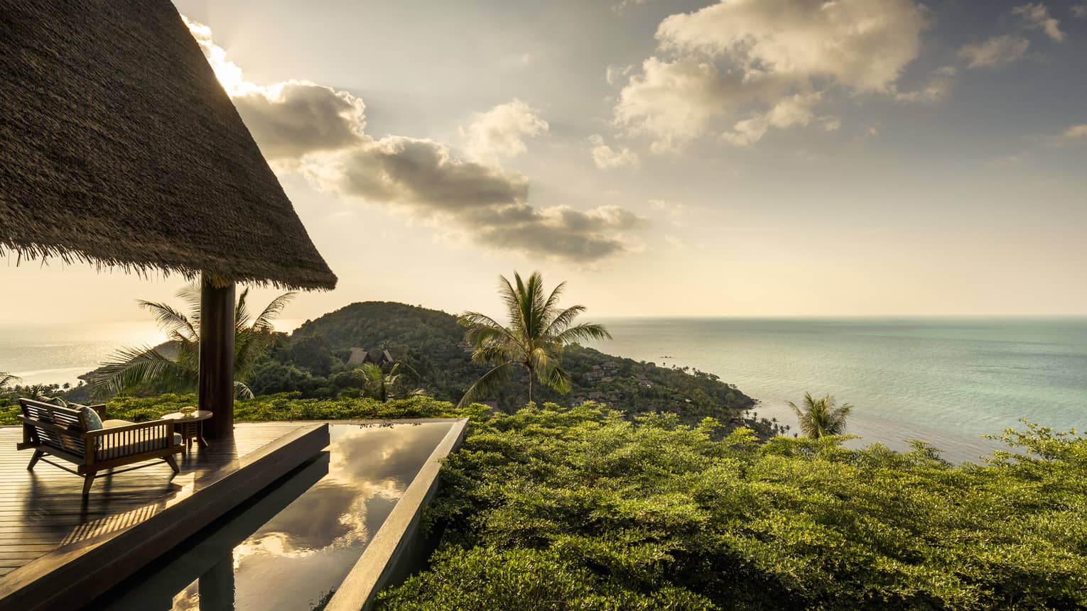 Patio lounge chair, thatched roof and deck overlooking canopy of tropical trees, ocean