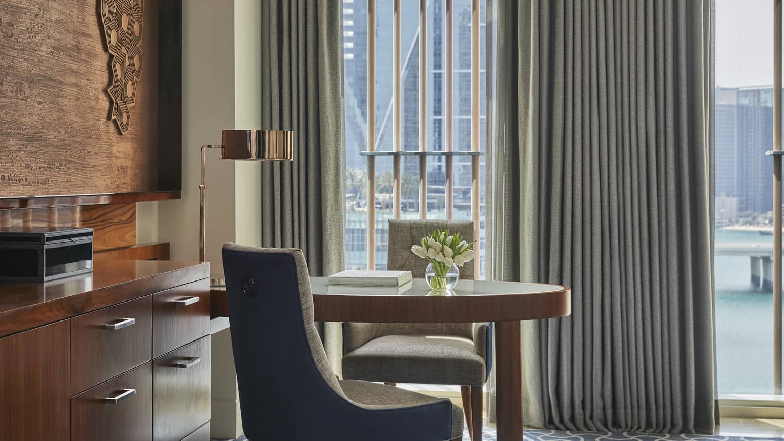Elegant workspace in a hotel room with a wooden desk, modern chair, tulip centerpiece and floor-to-ceiling windows overlooking a cityscape