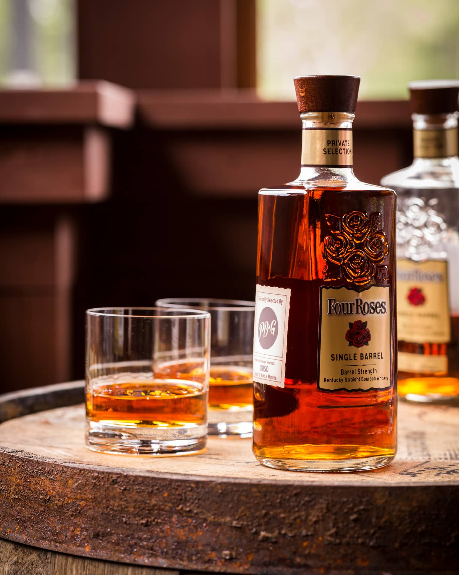 A bottle of whiskey and two glasses on a barrel. 