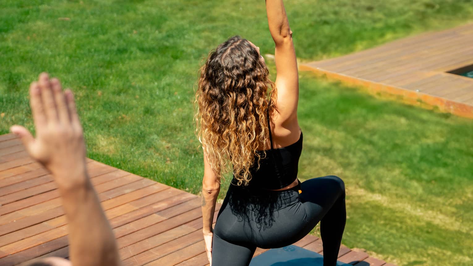 Two people in yoga pose practise on outdoor wooden deck overlooking lush green grass