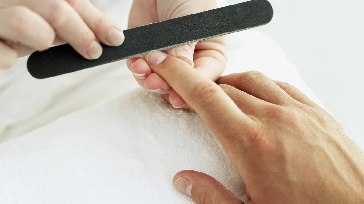 Woman holds manicure nail file to man's fingernails over white towel