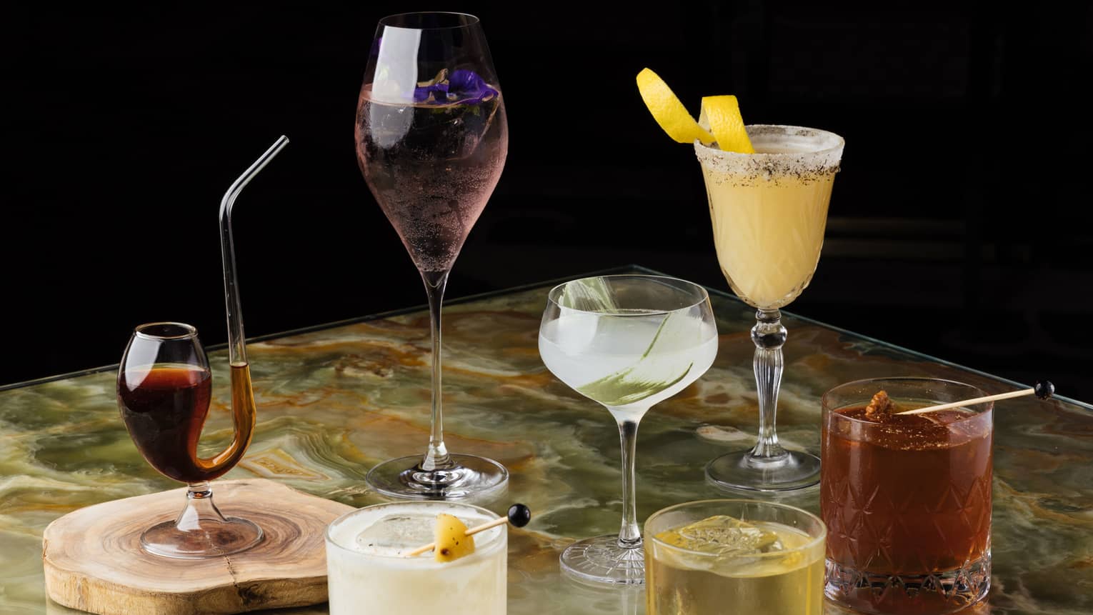 Seven cocktails in assorted glassware on marble table