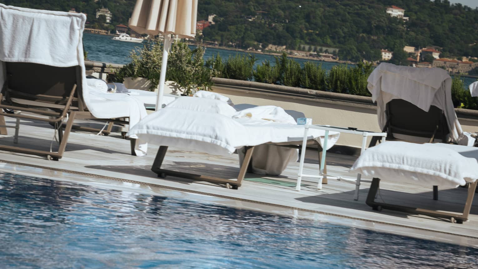 A person in a bathing suit and sunglasses at the edge of a clear blue pool. Lounge chairs, umbrellas and the distant landscape are in the background