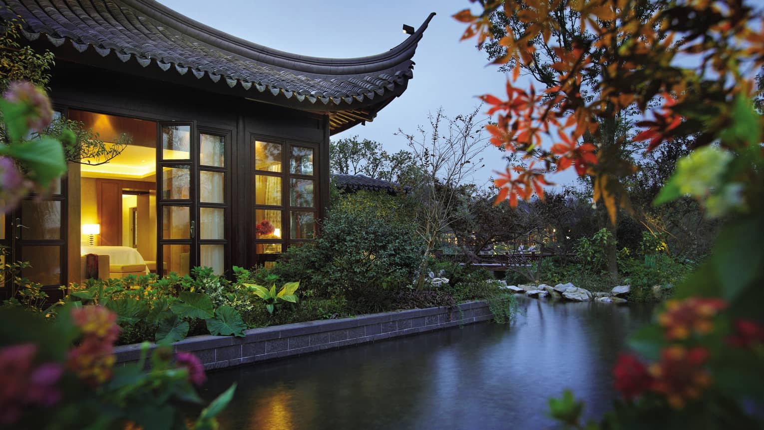 Side view of Lake Suite villa with sweeping roof, garden over water at night 