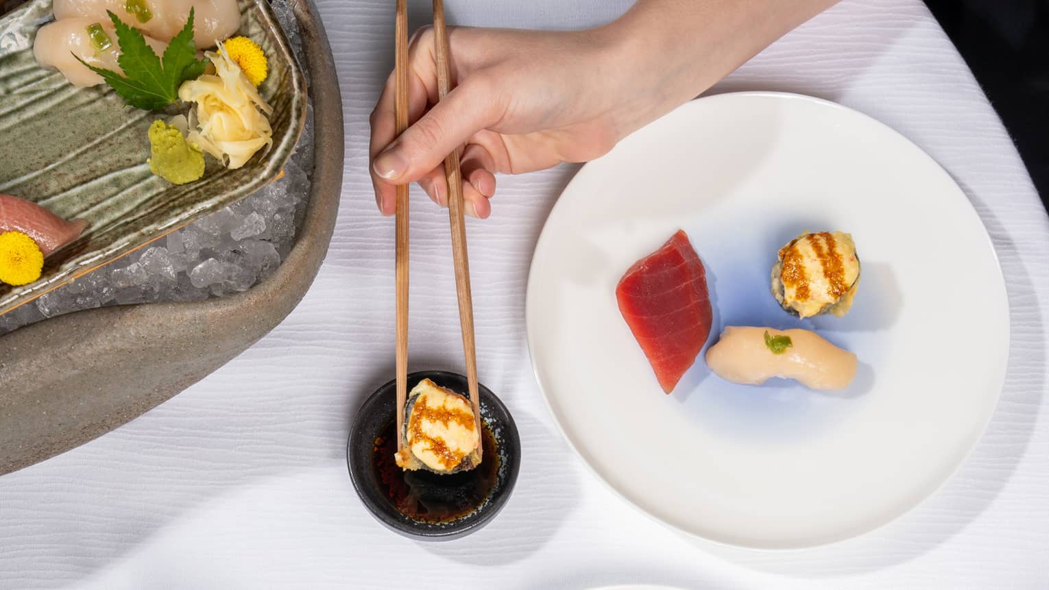 Overhead view of two white plates of sashimi and nigiri pieces along with an iced platter of more sushi