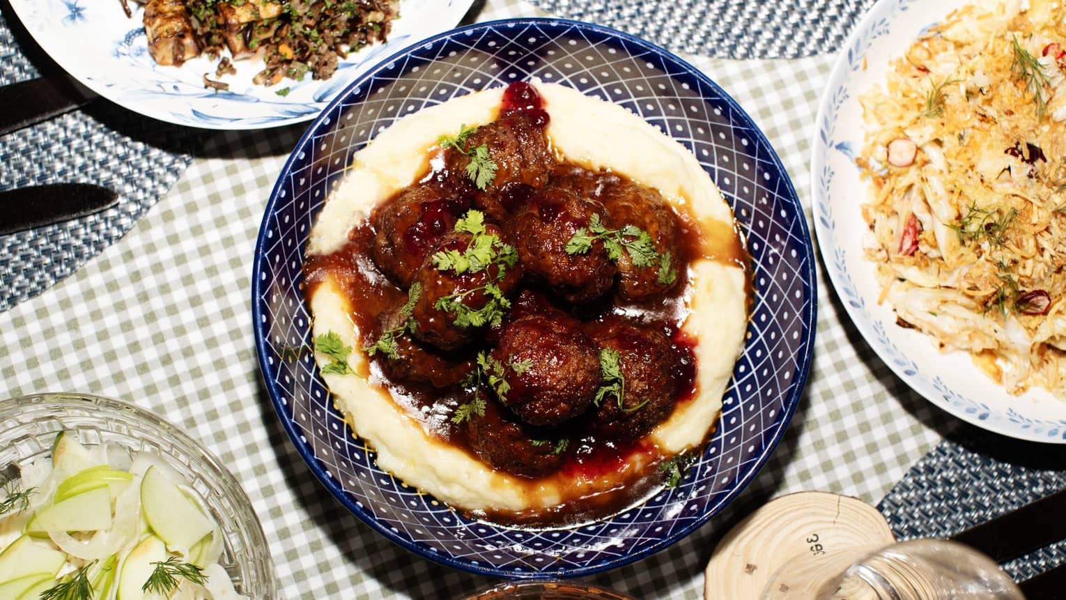 A meatball dish served over mashed potatoes, topped with a brown sauce and garnished with fresh green herbs