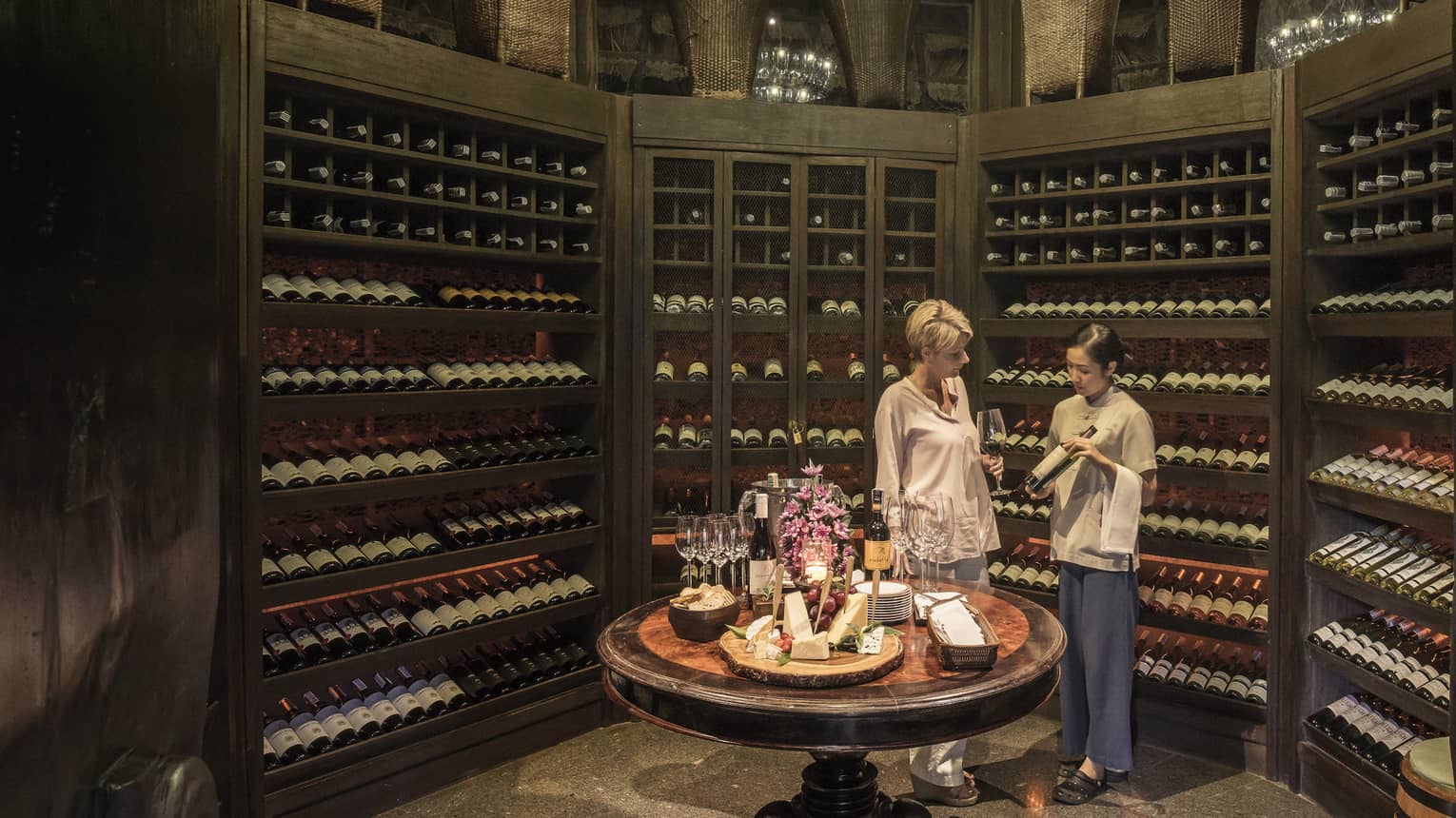 Two people examine wine bottles in Camp Wine Cellar