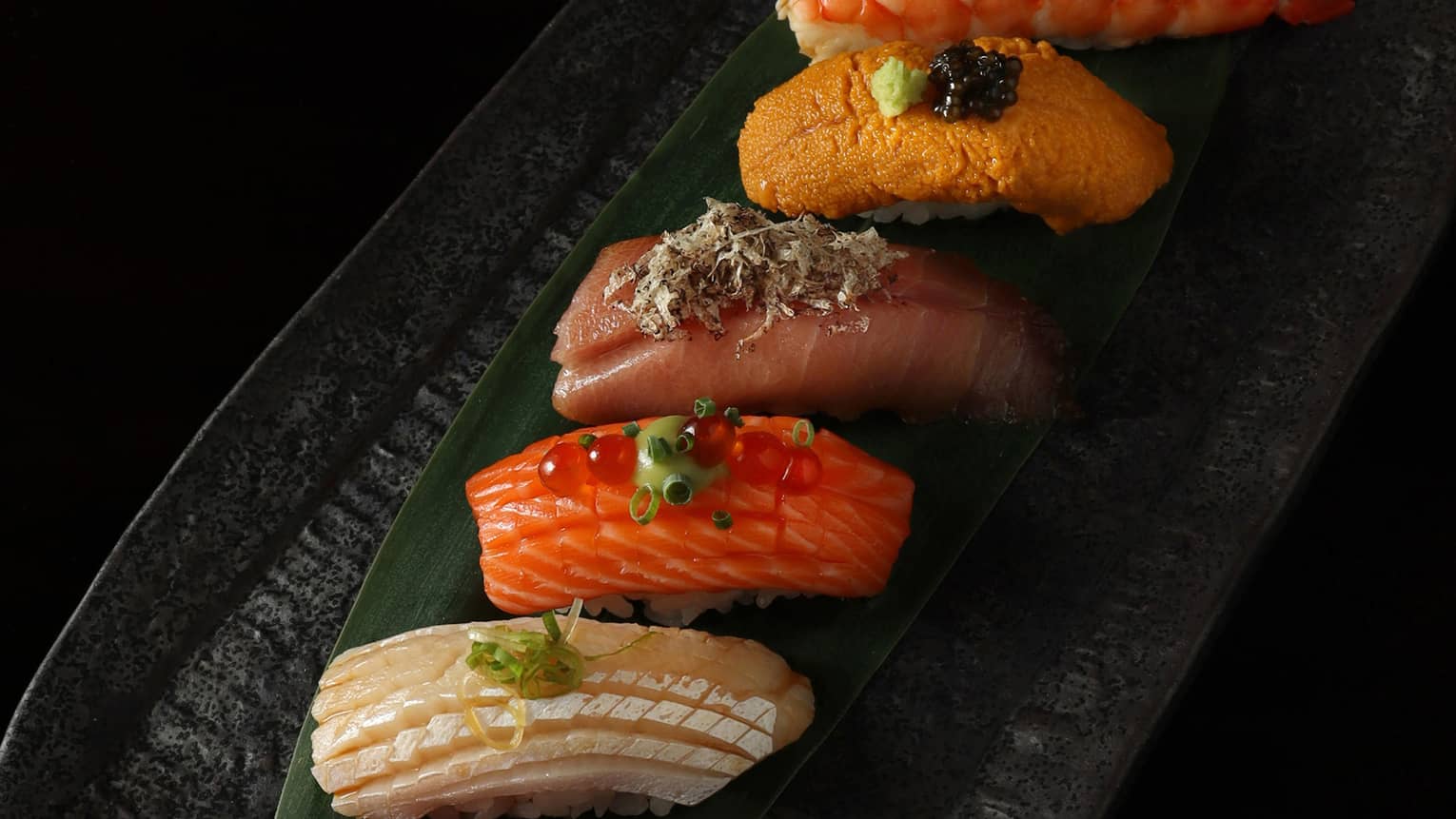 A row of different sushi on a black plate.