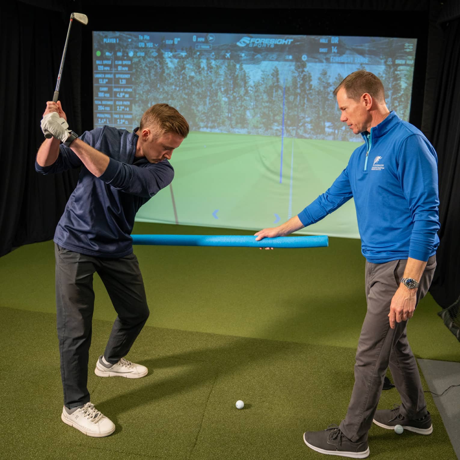 Two guests at a golf simulator, one guest swinging a golf club