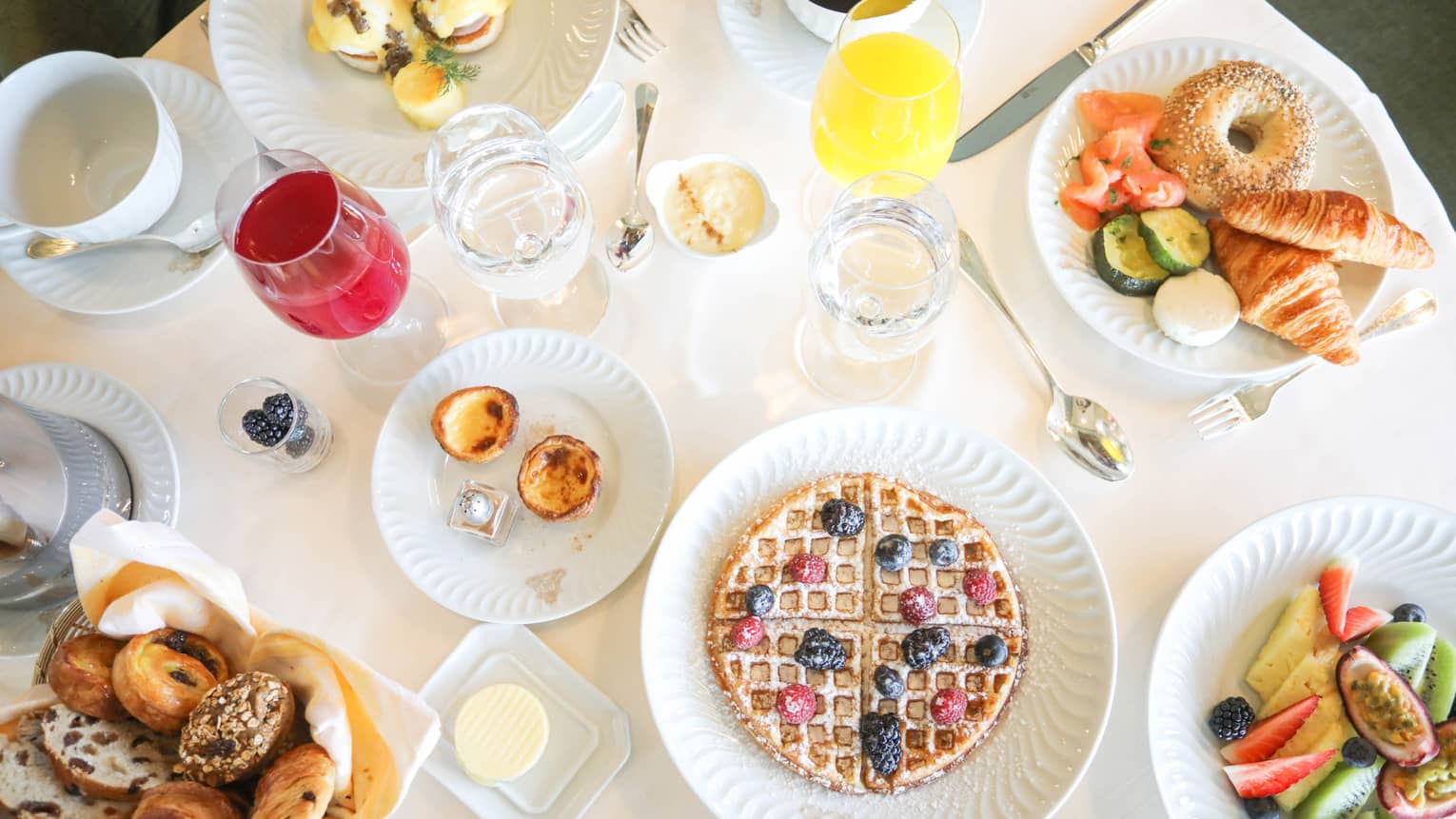 Aerial view of breakfast table with waffles, fresh fruit, pastries and juice in wine glasses