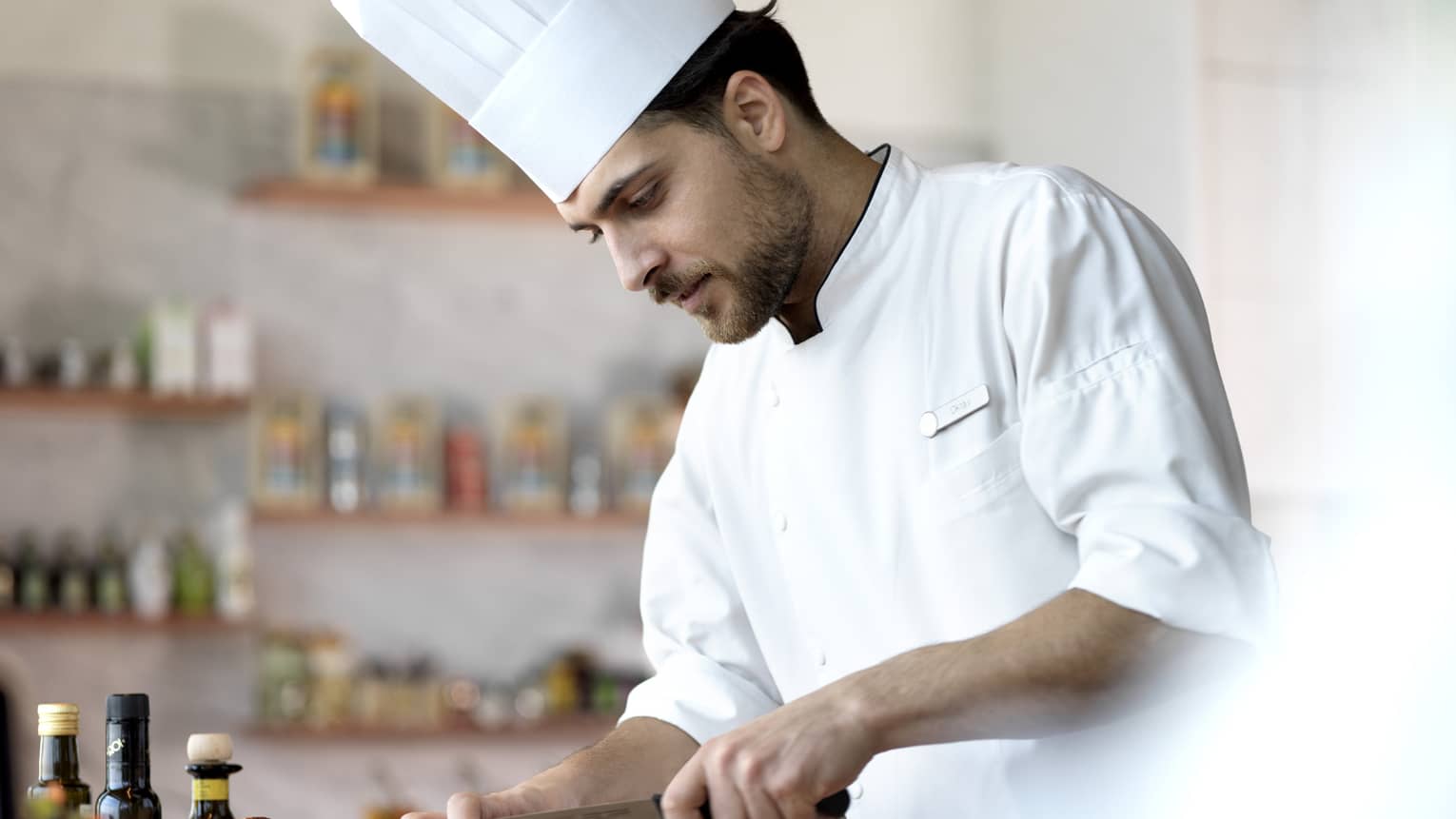 A chef in a white uniform, slicing through bread.