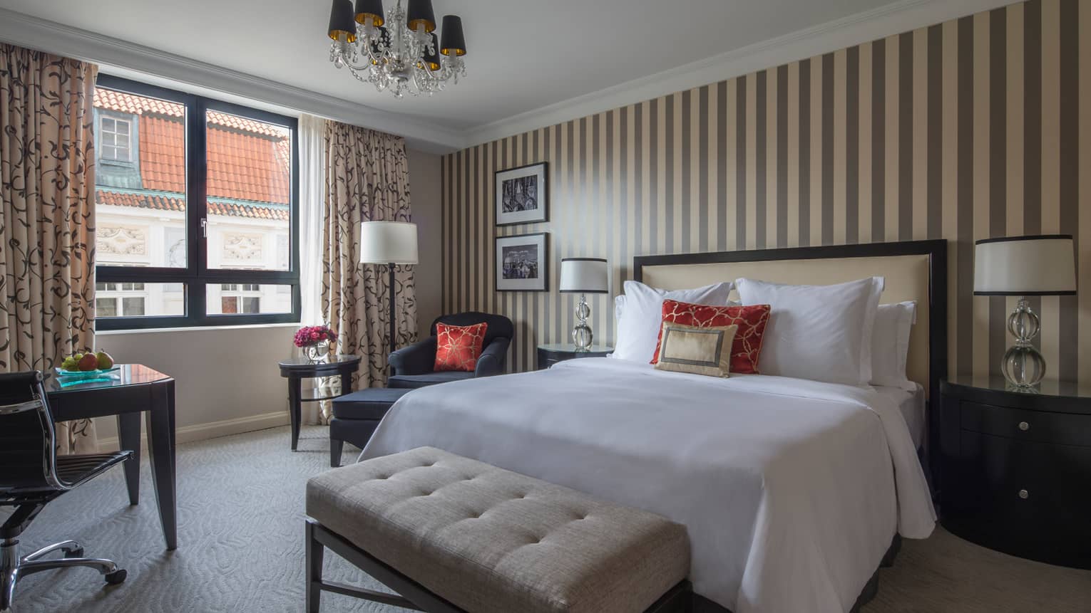 Deluxe Room bed, plush bench at foot, black-and-cream striped wallpaper, sunny windows