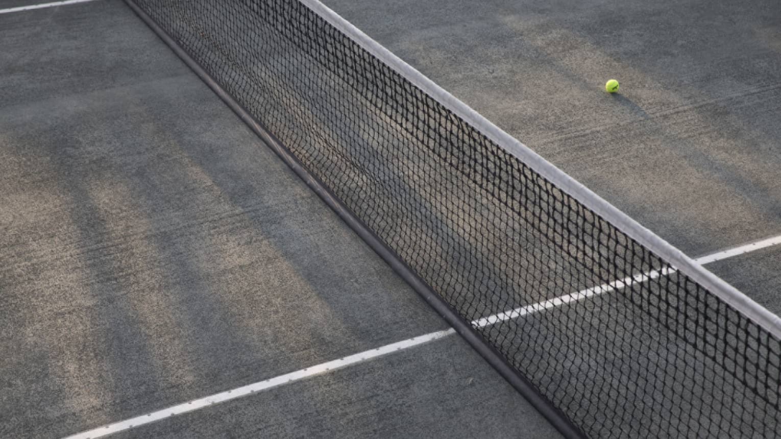 A lone tennis ball lies near the net on an empty court