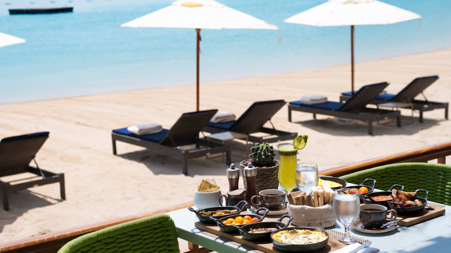 Patio dining table with breakfast items in front of sunny beach, lounge chairs