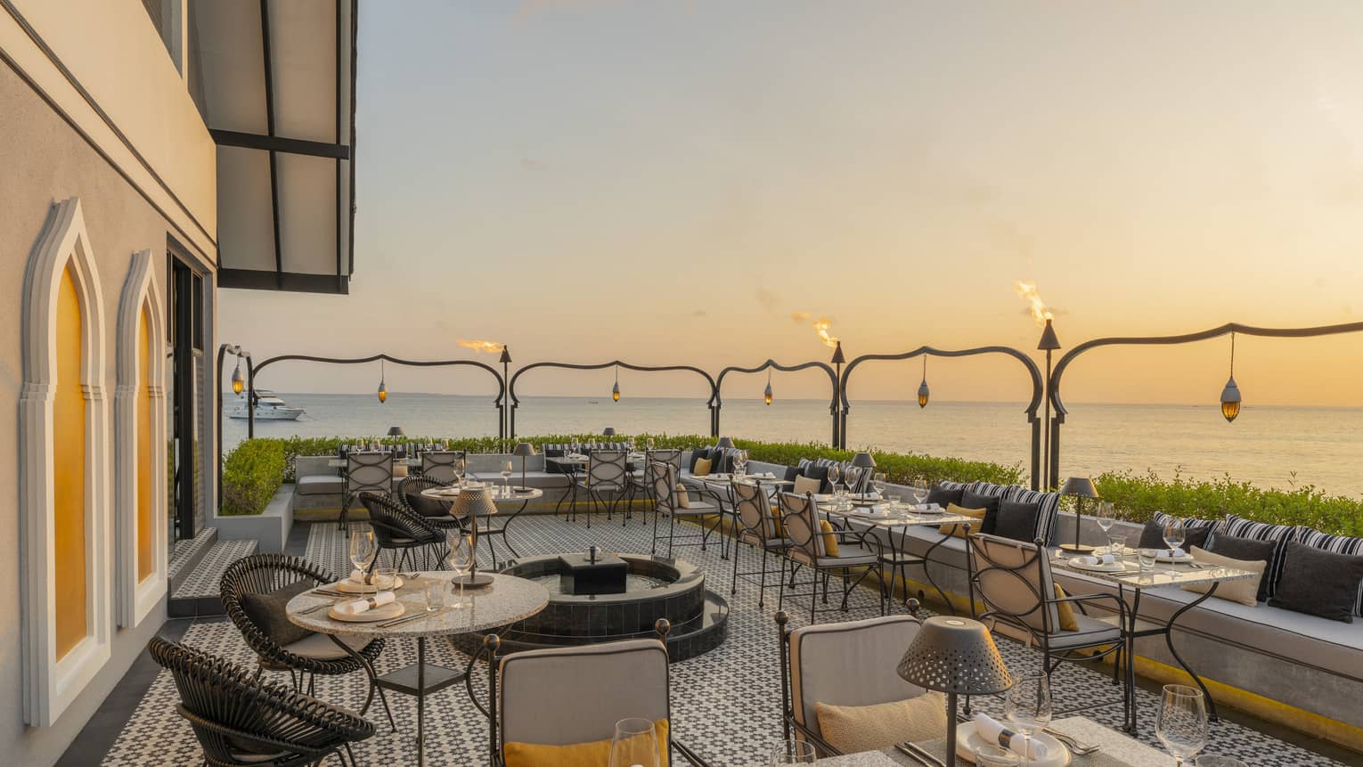 Outdoor terrace of Al Barakat at sunset with round and square tables, rattan chairs, string lighting