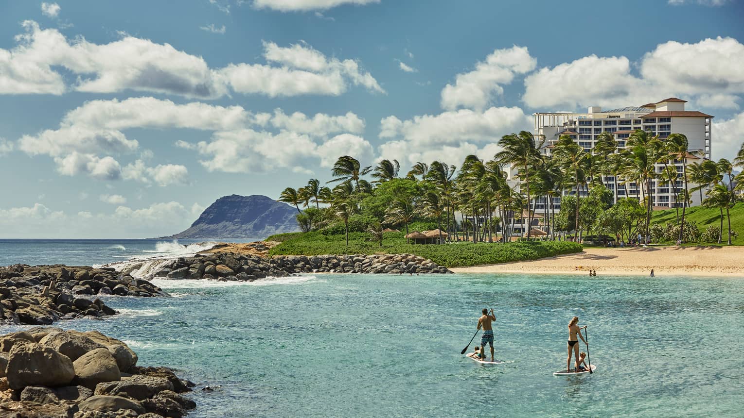 Two people on stand-up paddleboards in lagoon with beach and resort in background