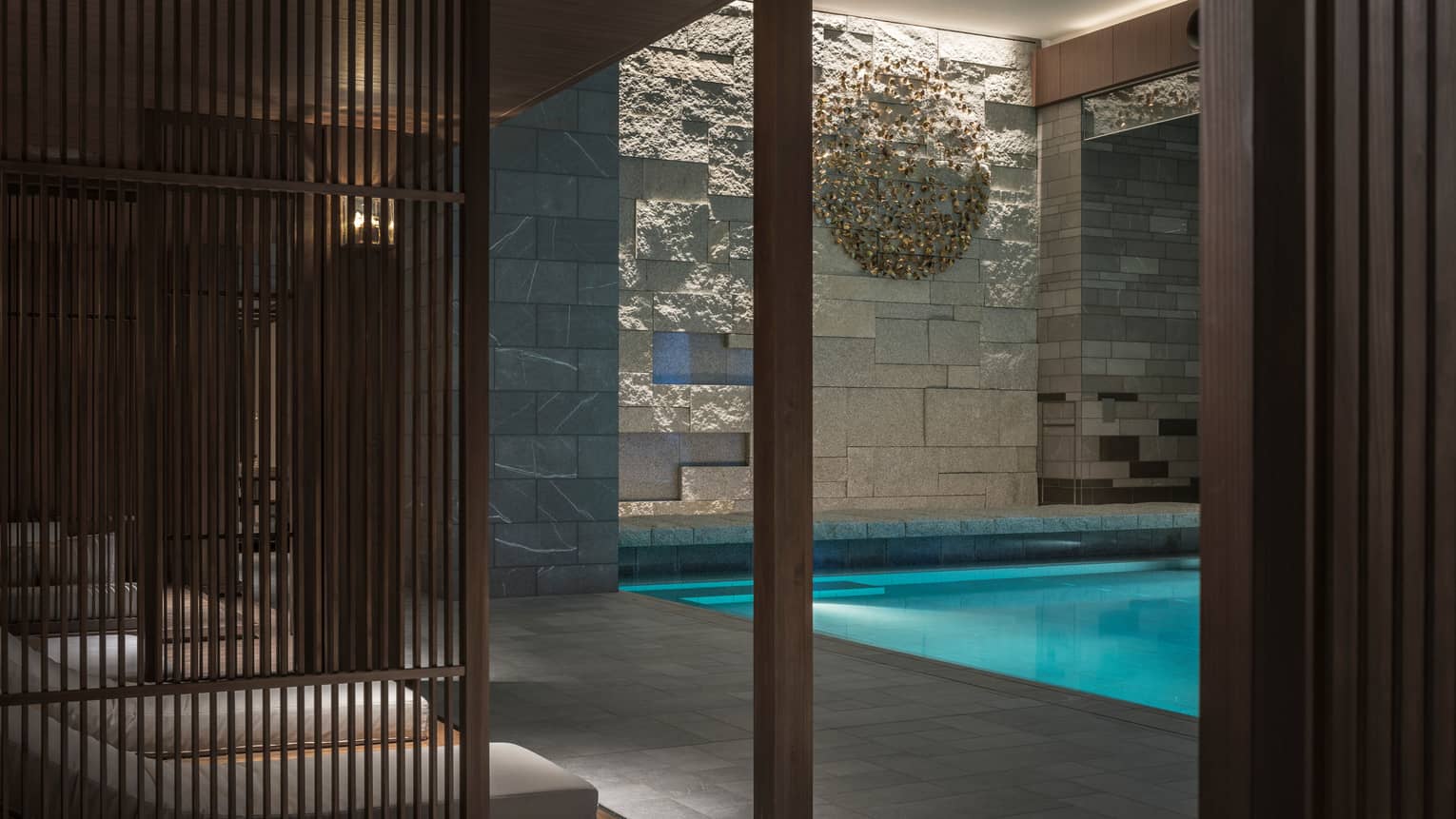 Lounge chairs behind wood wall, by indoor swimming pool under granite rock wall