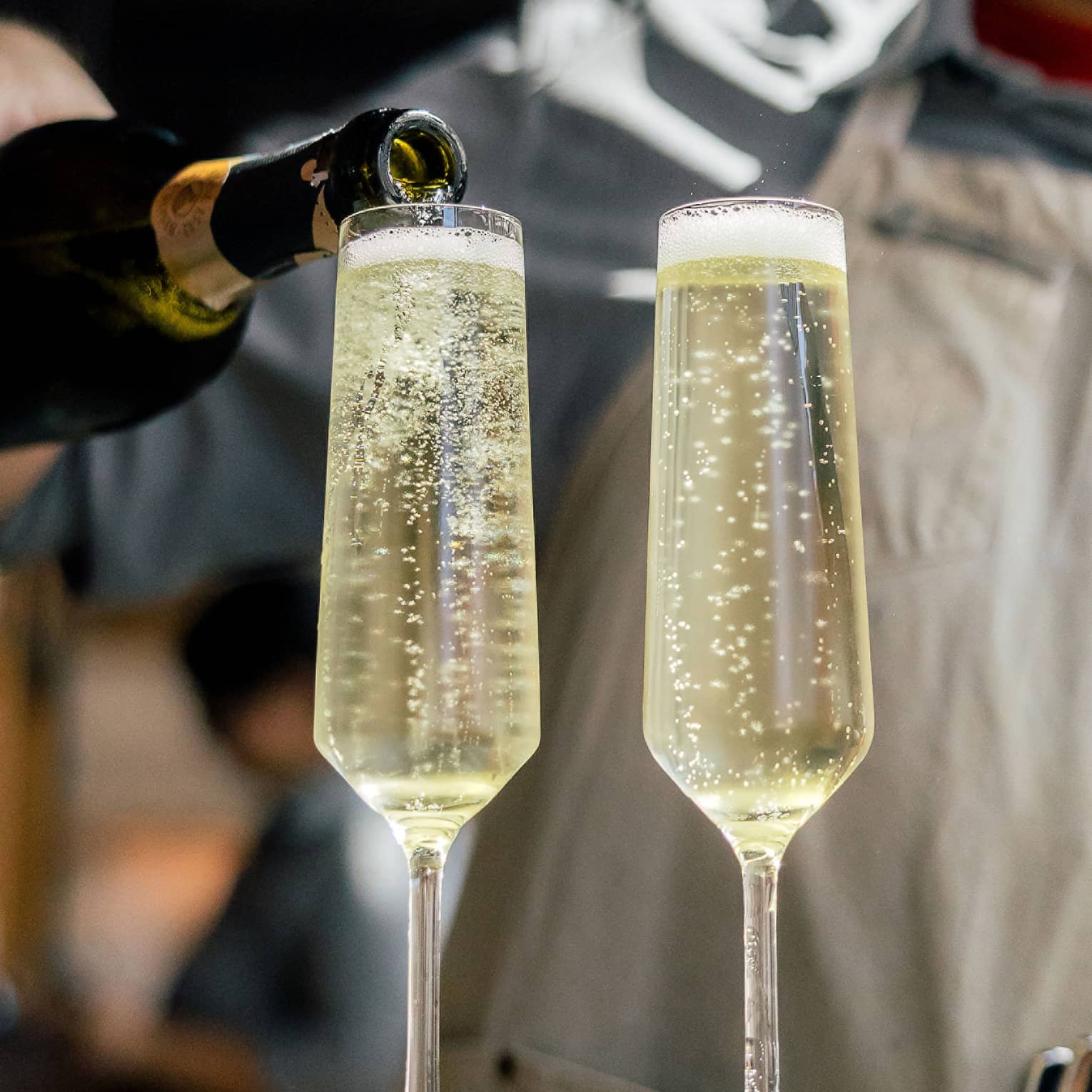 Person wearing an apron and pouring champagne into two glasses