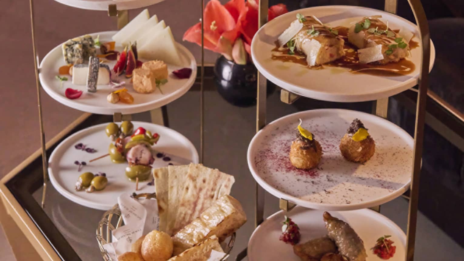 Tiered white and gold trays with a variety of savoury food of meats, cheese, olives, bread and pastries laid out on a table.