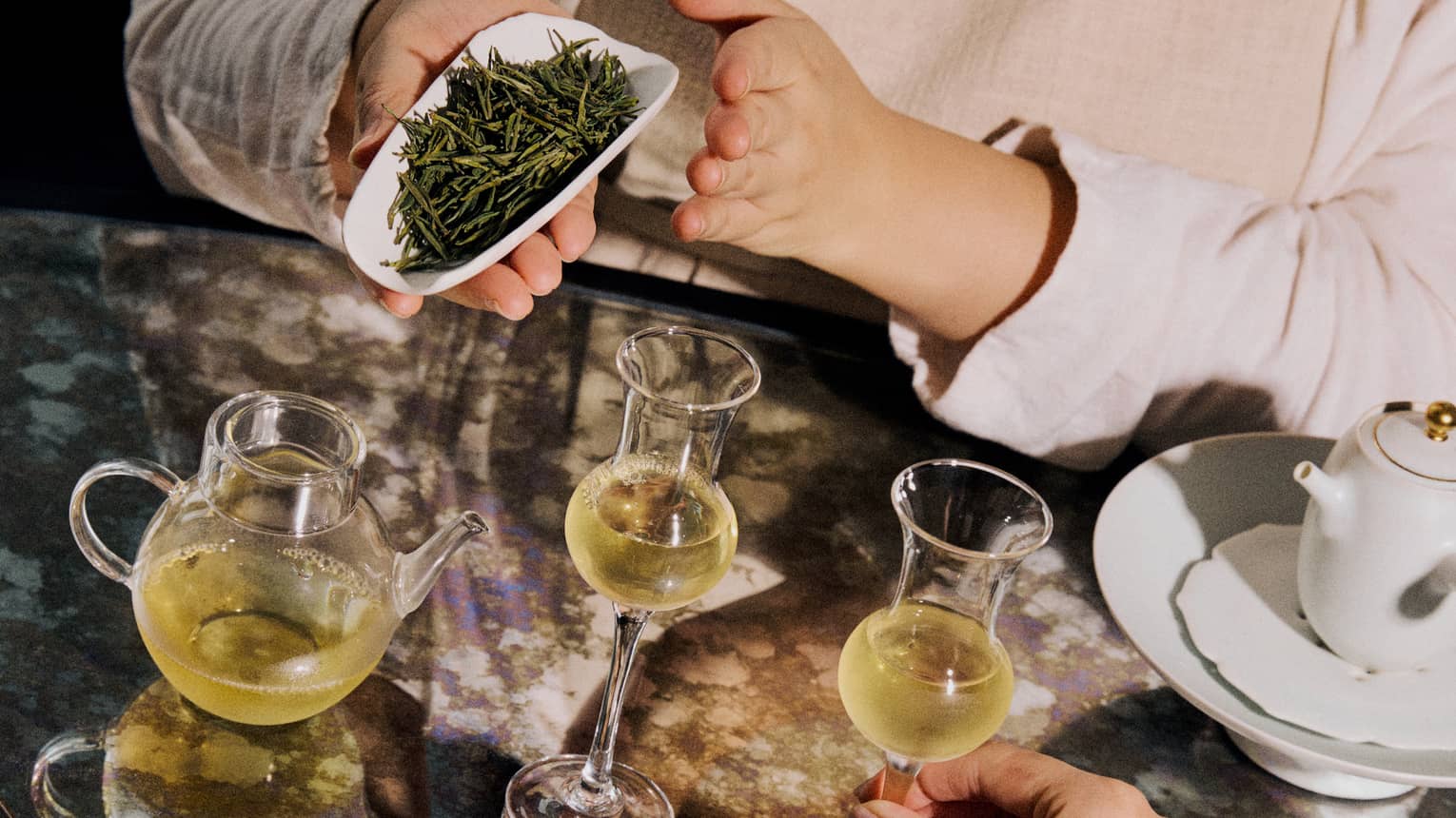 Loose leaf green tea displayed alongside two clear glasses of tea and a teapot.