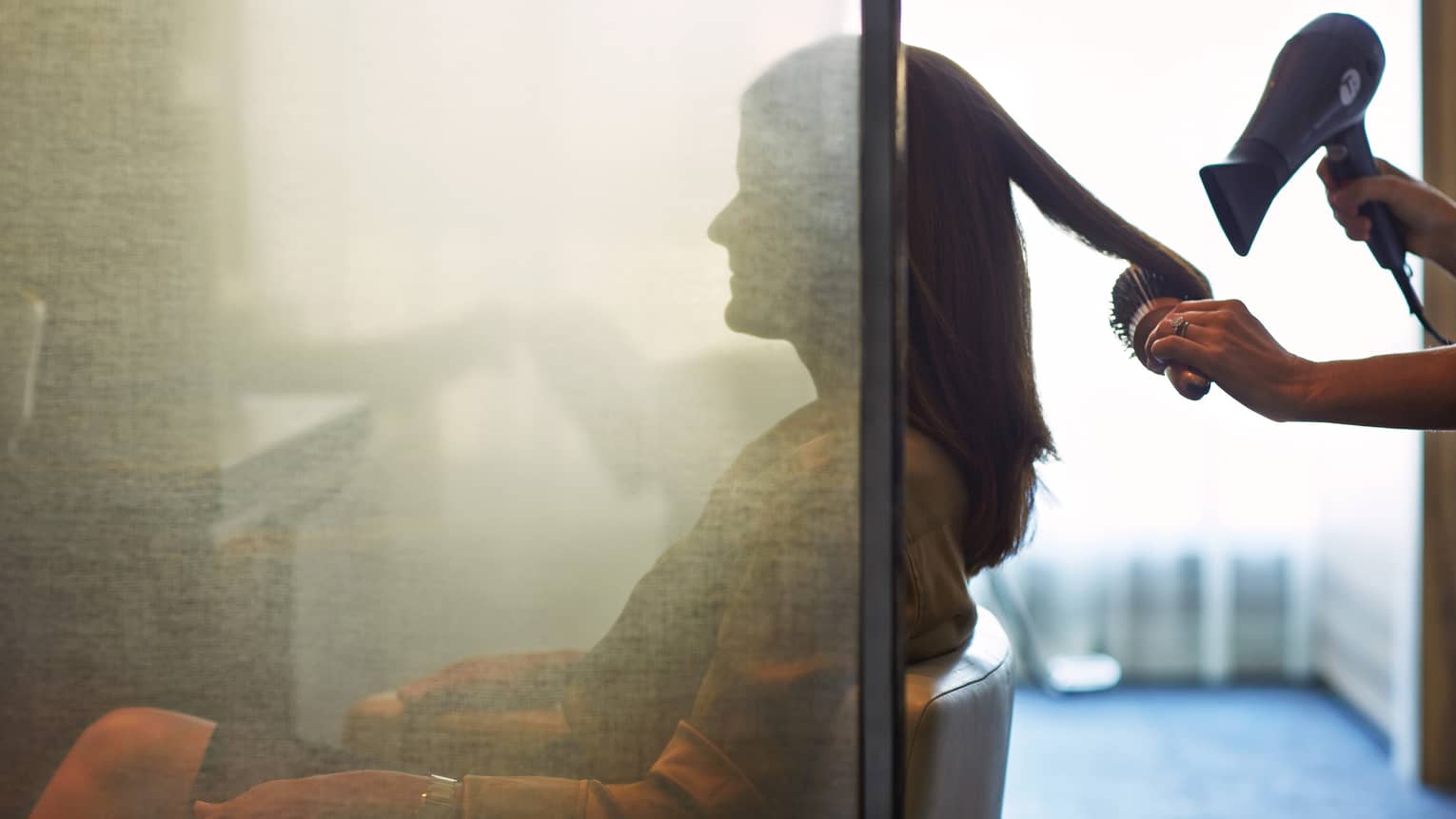 Silhouette of woman behind salon screen as hairdressers brushes, blow dries hair