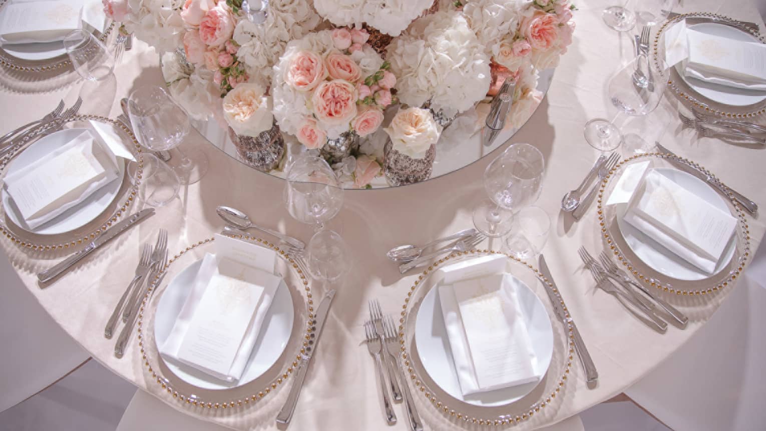 Aerial view of round wedding banquet table with pink roses, linens, menus on plates 