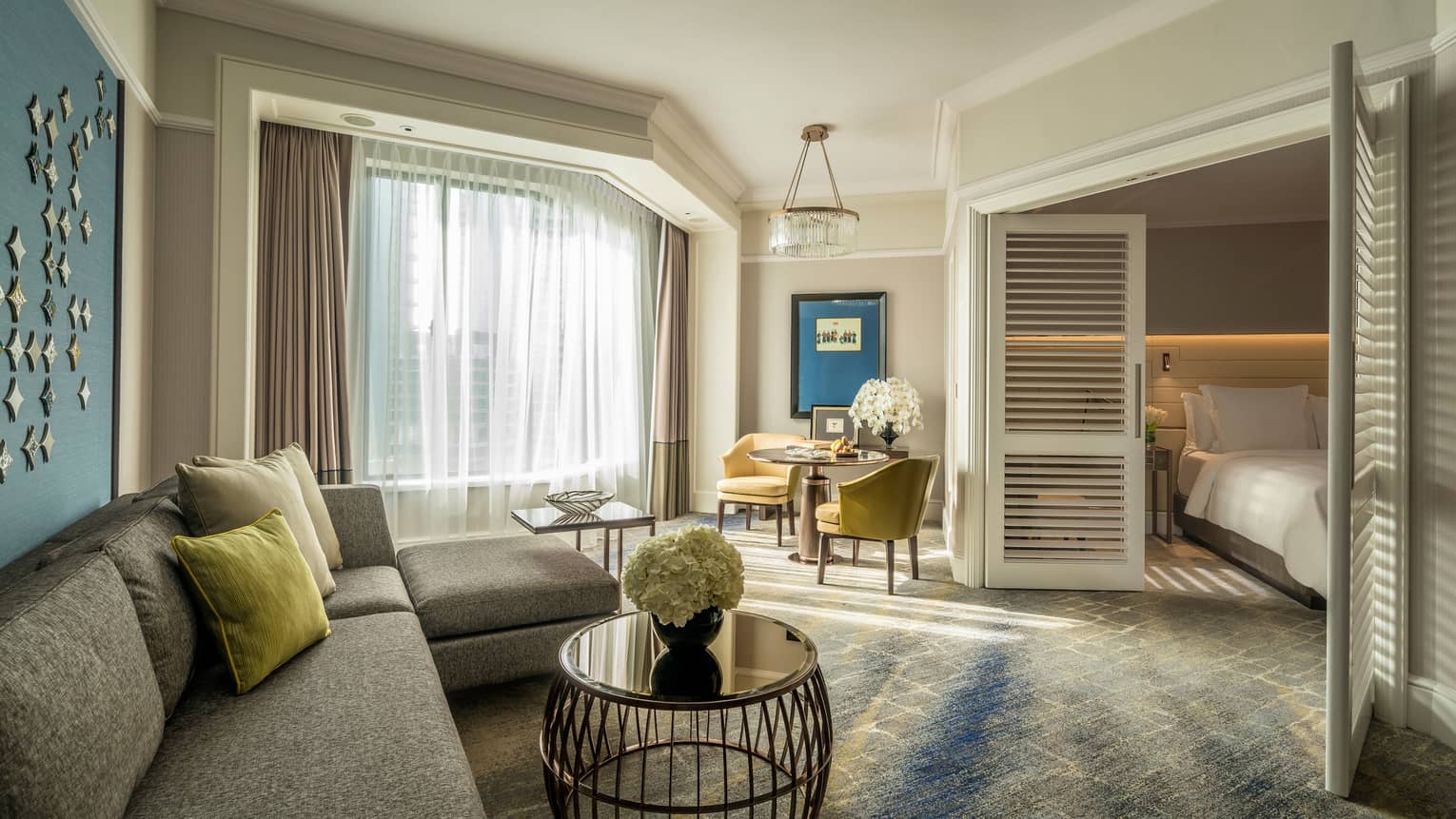 Four Seasons Executive Suite L-shaped sofa by sunny window with white curtains, table, wood shutters