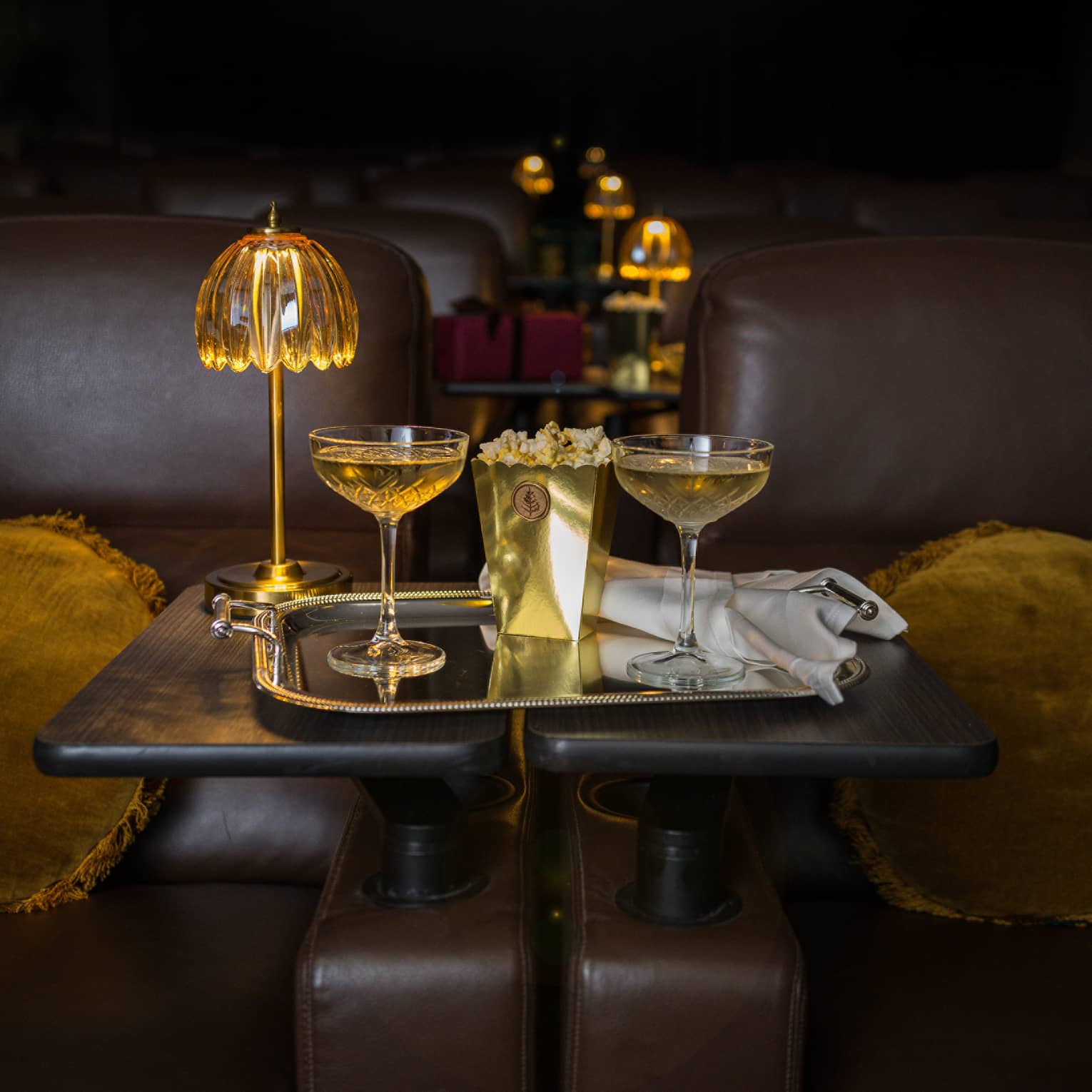 Two filled coupe glasses on a silver serving tray with popcorn in front of a golden dome light.