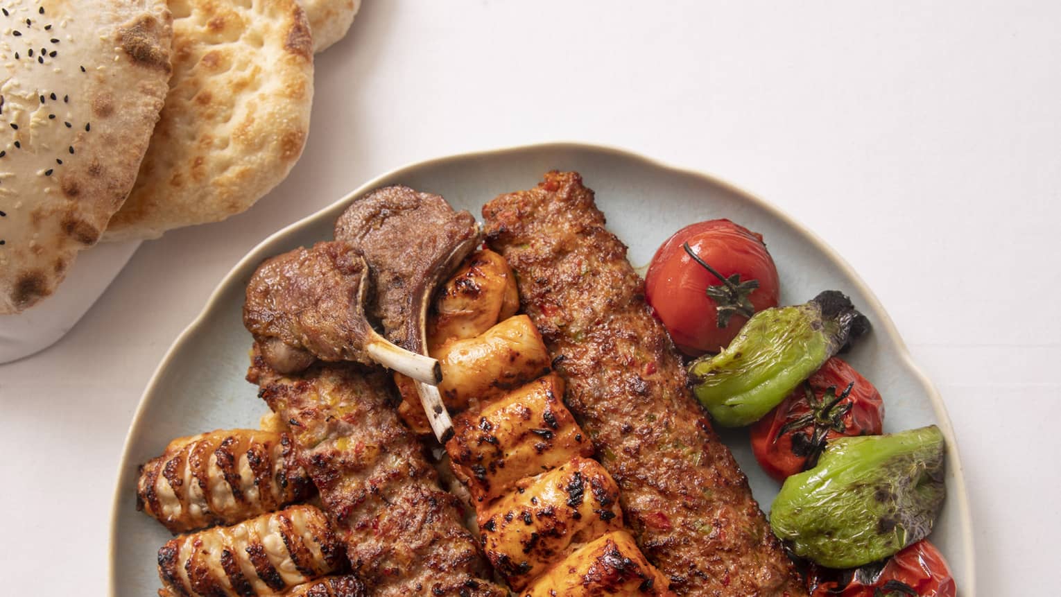 Grilled meat skewers and vegetables on round plate beside flatbread