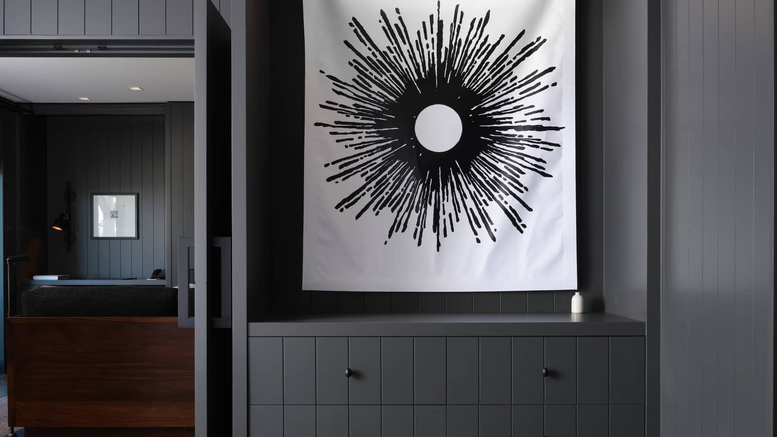 Black and white sun-like artwork hanging above a cabinet in a dark-paneled room of a luxury resort suite 